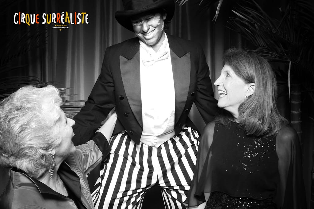 a circus performer on stilts poses in a photo booth with two women smiling up at them